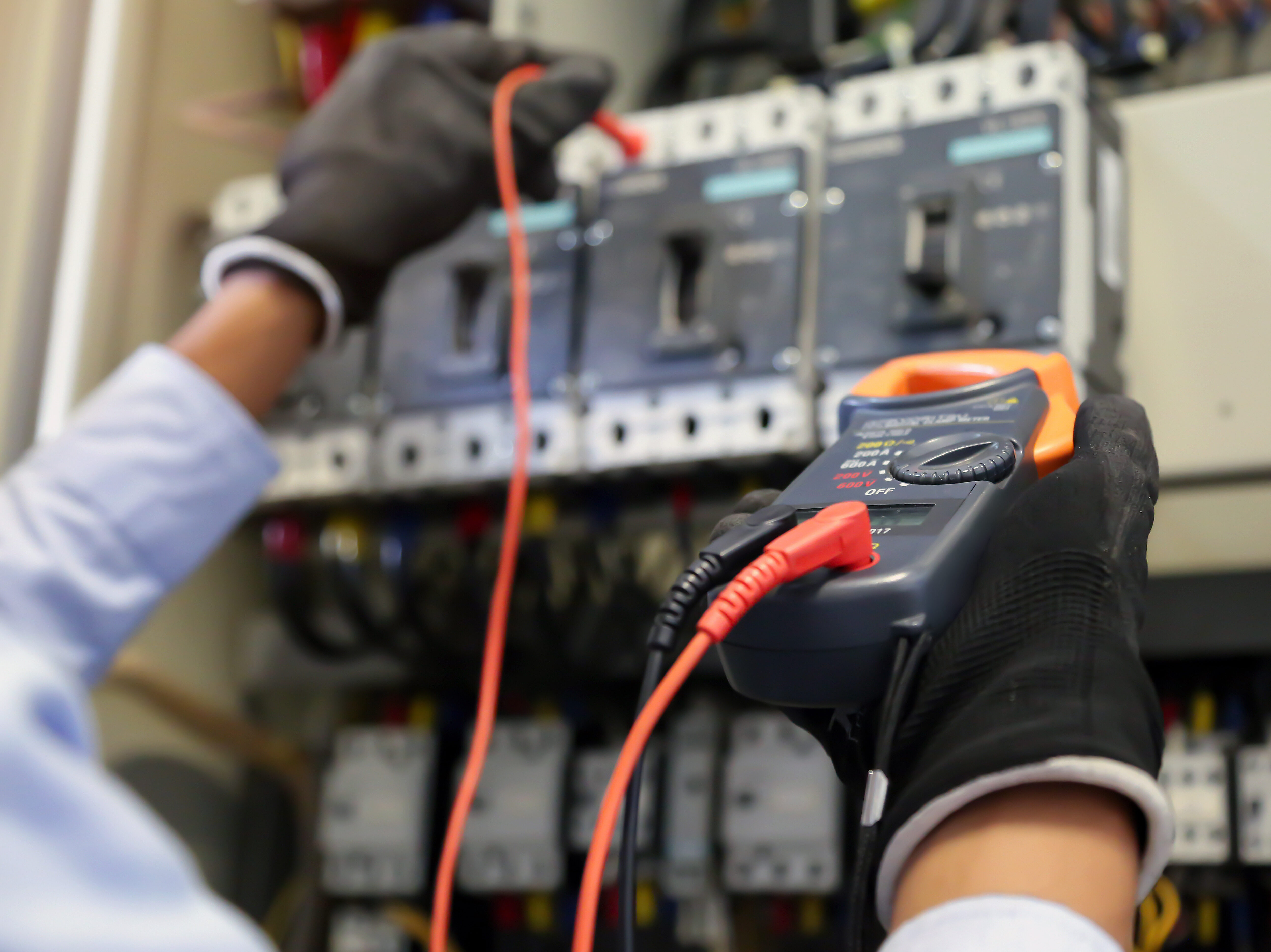 Electrical engineer using measuring equipment to checking electric current voltage at circuit breaker and cable wiring system for maintenance in main power distribution board.